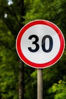 Road sign speed limit 30 kilometers per hour on green forest background with selective focus photo