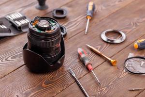 half-disassembled camera zoom lens on wooden table surrounded with tools photo