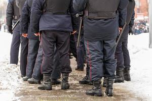 Russian police officers legs in black ankle boots, red stripe pants and with rubber tonfa night sticks. photo