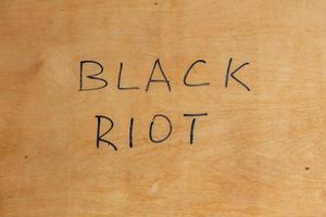 The words black riot handwritten with black paint marker on flat plywood surface. Concept. photo