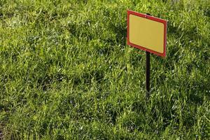 blank yellow sign mockup on green lawn background - close-up with selective focus photo