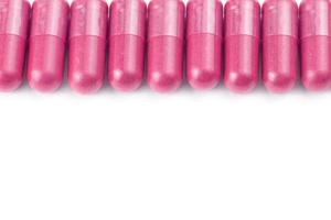 row of plastic pink color organic capsules isolated on white background closeup with selective focus photo