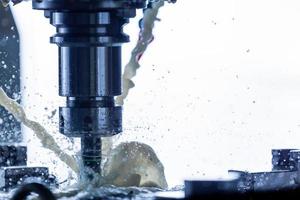 Close-up view of vertical cnc steel milling process with external water coolant streams, splashes and a lot of metal chips, high contrast photo
