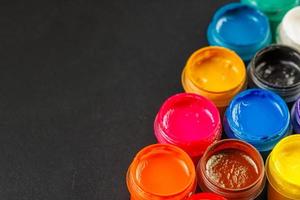 close-up background of opened small gouache paint jars on black surface photo