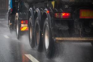 Rain water splash flow from wheels of heavy truck moving fast in daylight city with selective focus. photo