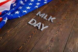 the word MLK day laid with silver metal letters on wooden surface with crumpled USA flag at left side photo