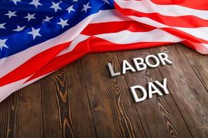 words labor day laid with silver metal letters on wooden surface with crumpled USA flag on left side photo