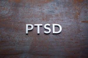 the word PTSD laid with silver metal letters on flat rusted steel sheet background in straight perspective photo