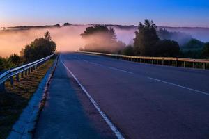 dence early morning fog in wold at summer highway near river with guard rails photo