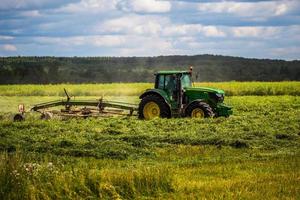 TULA, RUSSIA JULY 30, 2019 green haymaking tractor on summer field before storm - telephoto shot with selective focus photo