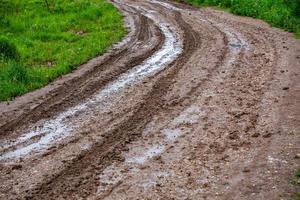 dirty clay mud road turn with puddles and tire tracks - closeup with selective focus and linear perspective photo