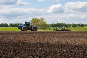 tractor azul con ruedas dobles tirando de la grada de discos con cesta de rodillos en un día caluroso y soleado foto