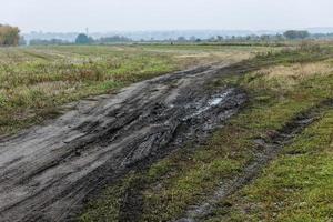 Mañana neblinosa otoñal paisaje rústico con camino de tierra en primer plano y pequeños edificios en la colina al fondo foto