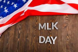 the word MLK day laid with silver metal letters on wooden surface with crumpled USA flag at upper side photo