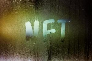 the word NFT - non-fungible token handwritten on foggy window glass at night photo