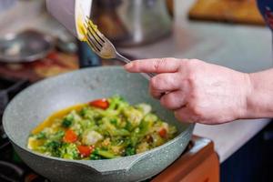 las manos femeninas agregan yemas de huevo revueltas para freír verduras mientras cocinan tortillas foto