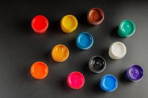 close-up background of opened small gouache paint jars on black surface photo