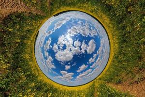 esfera azul vista invertida del pequeño planeta del campo de colza floreciente amarillo, vista del túnel redondo foto