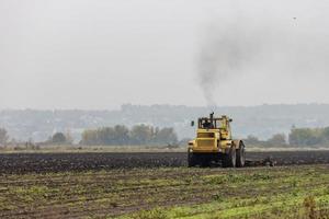 grim yellow tractor plows the field after harvest before winter at cloudy and foggy autumn morning photo