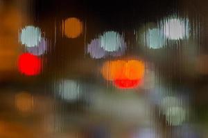 an abstract background of red and brown lights bokeh trough wet glass at night close-up with selective focus photo