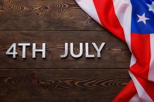 las palabras 4 de julio y la bandera de estados unidos arrugada sobre fondo de superficie de madera con textura plana foto