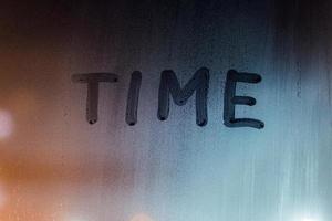 the word time handwritten by finger on night wet window glass photo