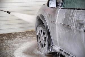 un proceso de enjuague con espuma de jabón en la rueda de camión plateada con chorro de agua a presión en la estación de lavado de autos interior de autoservicio foto
