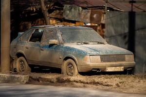 Old dirty abandoned car on sideroad with thick layer of mud and broken window at daylight. photo