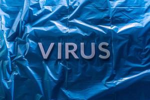 la palabra virus se colocó con letras de metal plateado en una película de plástico azul arrugada con una luz dramática foto