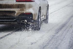 Road snow pieces flow from wheels of dirty white car moving fast in daylight city with selective focus. photo