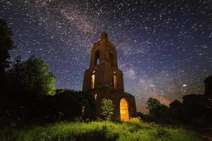 ruina del campanario nocturno en el bosque en la noche estrellada con luz interna foto