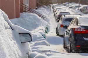 cars buried under snow in parking near residental building at sunny day light photo