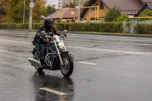 hombre en bicicleta chopper negra moviéndose en el camino húmedo del suburbio de otoño foto