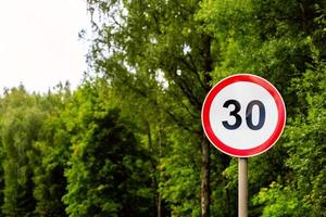 Road sign speed limit 30 kilometers per hour on green forest background with selective focus photo