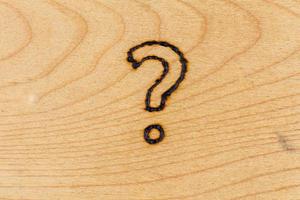 question mark drawn with handheld woodburner on flat wooden surface photo