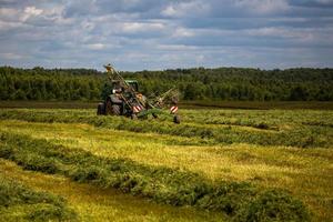 green haymaking tractor on summer field before storm - telephoto shot photo