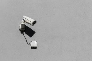 small white surveillance camera on flat gray matte plaster wall photo