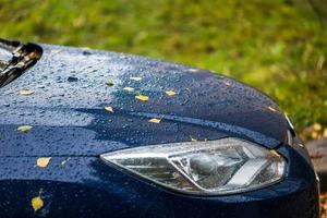 coche azul en el clima lluvioso de otoño con hojas de abedul naranja - enfoque selectivo ganar desenfoque de primer plano foto