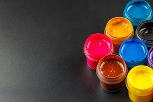 close-up background of opened small gouache paint jars on black surface photo