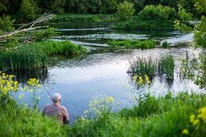 old man fishing with friend on a river at summer daytime with selective focus photo