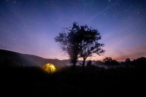 yellow tent under tree at summer starry night with fog photo