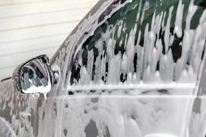 Closeup view of motor car window with layer of soap sud during car wash. photo