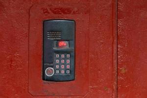 An intercom on old painted red steel surface with a keypad, digital display and rfid sensor for calling close-up photo