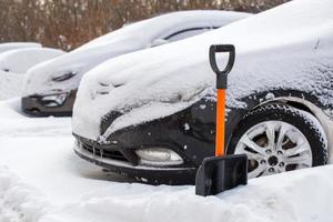 plastic snow shovel in front of snow-covered car at sunny winter morning photo