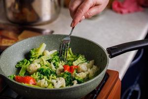 mujer mayor caucásica mano con tenedor recoge verduras para freír en una sartén foto