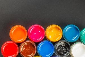 close-up background of opened small gouache paint jars on black surface photo