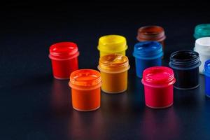 close-up background of opened small gouache paint jars on black surface photo