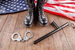 silver handcuffs, black boots and police baton near US flag on wooden surface photo