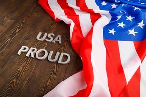 words USA proud laid with silver metal letters on brown wooden surface with flag of United States of America photo