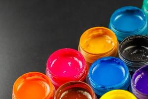 close-up background of opened small gouache paint jars on black surface photo